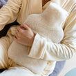 Load image into Gallery viewer, Hot water bottle cover made from sheepskin being hugged in a cosy setting with pyjamas.