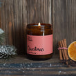 Load image into Gallery viewer, A lit Christmas scented candle with a label that reads 'Christmas', alongside cinnamon sticks and a slice of orange, against a wooden background.