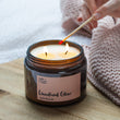 Load image into Gallery viewer, Velvety chocolately woods are the notes that make this winter warmer candle so popular. Unisex, appealing to both men and women, this scent is perfect for Autumn. It is great for the bedroom. Features warming notes such as chocolate, vetiver, warm spices, and nutmeg. Woodland Glow Double Wick Long Lasting Candle being lit by a luxury match