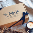 Load image into Gallery viewer, the top of the the hand made candle gift box featuring a black tied cotton ribbon and a lit natural-wax candle.