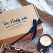 Load image into Gallery viewer, Hand made candle gift box featuring a black tied cotton ribbon and a lit natural-wax candle.