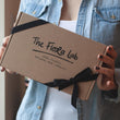Load image into Gallery viewer, the top of the the hand made candle gift box featuring a black tied cotton ribbon and a lit natural-wax candle.