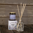 Load image into Gallery viewer, A reed diffuser set from The Flora Lab, featuring a glass bottle with natural reed sticks and a matching dark glass jar candle with a lavender label and floral-patterned box, set against a rustic wooden background.
