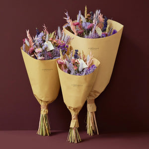 Purple Glow Dried Wild flower bouquet. 
Illuminate your space with the enchanting hues of the Purple Glow bouquet from our Autumn Collection. This hand-tied field bouquet combines soft pinks, lilacs, blues, and purples for a magical and elegant display.

This bouquet contains: Light pink oats, natural wheat, lilac wheat, blue delphinium, Odillia spray roses, lavender statice, blue statice, purple limonium, pink acroclinium/rhodanthe, milka shola, and milka broom bloom.