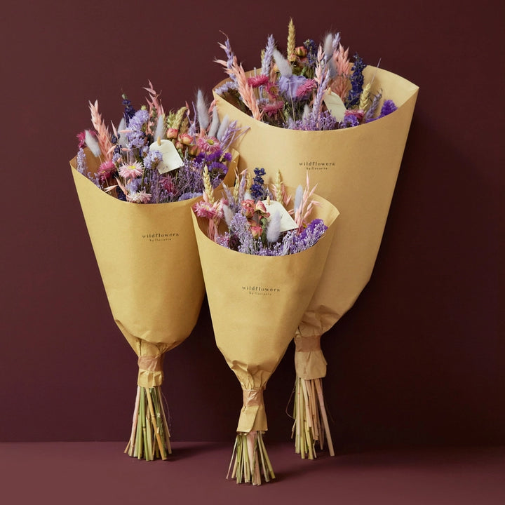 Purple Glow Dried Wild flower bouquet. 
Illuminate your space with the enchanting hues of the Purple Glow bouquet from our Autumn Collection. This hand-tied field bouquet combines soft pinks, lilacs, blues, and purples for a magical and elegant display.

This bouquet contains: Light pink oats, natural wheat, lilac wheat, blue delphinium, Odillia spray roses, lavender statice, blue statice, purple limonium, pink acroclinium/rhodanthe, milka shola, and milka broom bloom.