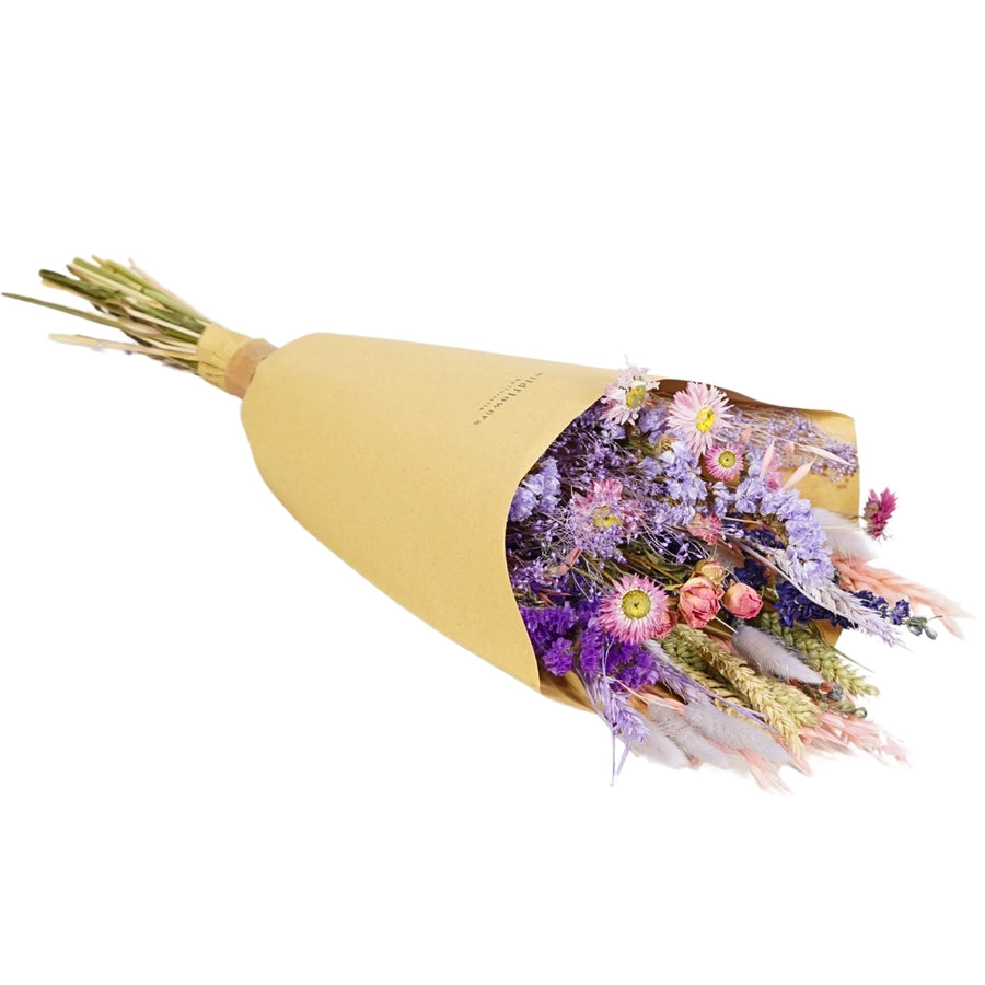 lose up of our dried wildflower purple glow bouquet 
Illuminate your space with the enchanting hues of the Purple Glow bouquet from our Autumn Collection. This hand-tied field bouquet combines soft pinks, lilacs, blues, and purples for a magical and elegant display.

This bouquet contains: Light pink oats, natural wheat, lilac wheat, blue delphinium, Odillia spray roses, lavender statice, blue statice, purple limonium, pink acroclinium/rhodanthe, milka shola, and milka broom bloom.