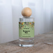 Load image into Gallery viewer, The Flora Lab Renaissance Man Hand Poured Room Perfume Spray in a clear glass bottle with a wooden ball lid, featuring a botanical label, resting on a rustic wooden surface

