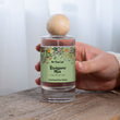 Load image into Gallery viewer, hands holding The Flora Lab Renaissance Man Hand Poured Room Perfume Spray with the gold pump nozzle visible and the wooden ball lid held separately, wearing a cream knit jumper
