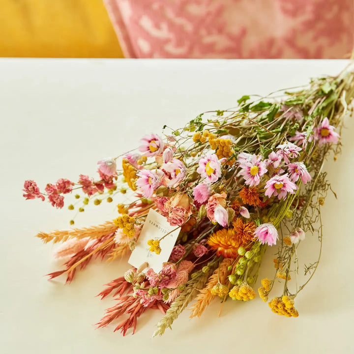 Pastel dried wildflower bouquet with pink daisies, yellow strawflowers, and wheat grass wrapped in kraft paper, perfect for sustainable home decor, wedding gifts, or bohemian floral arrangements
