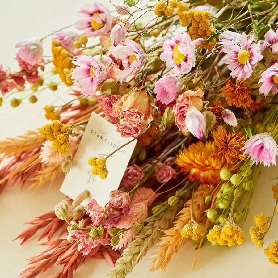 Pastel dried wildflower bouquet with pink daisies, yellow strawflowers, and wheat grass wrapped in kraft paper, perfect for sustainable home decor, wedding gifts, or bohemian floral arrangements