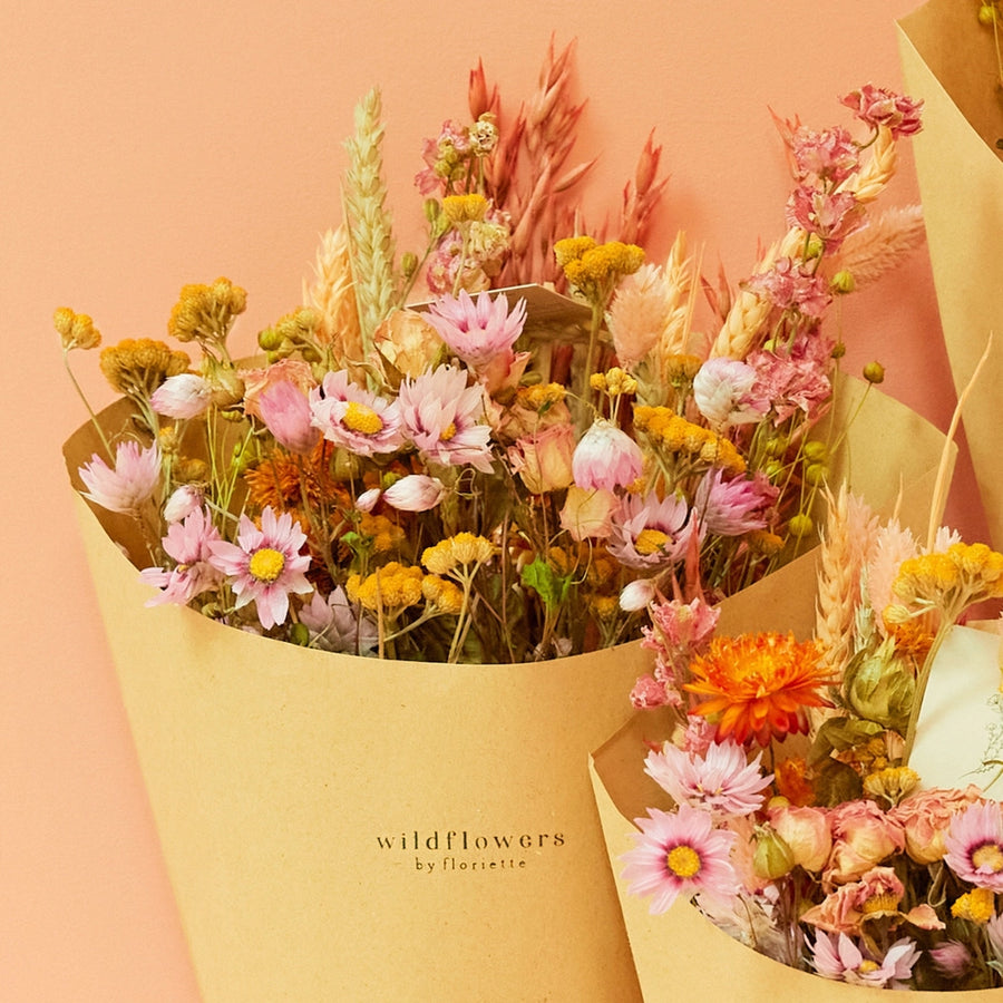 Pastel dried wildflower bouquet with pink daisies, yellow strawflowers, and wheat grass wrapped in kraft paper, perfect for sustainable home decor, wedding gifts, or bohemian floral arrangements