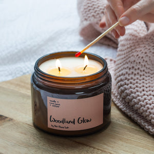 Velvety chocolately woods are the notes that make this winter warmer candle so popular. Unisex, appealing to both men and women, this scent is perfect for Autumn. It is great for the bedroom. Features warming notes such as chocolate, vetiver, warm spices, and nutmeg.  Woodland Glow Double Wick Long Lasting Candle being lit by a luxury match 