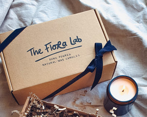 the top of the the hand made candle gift box featuring a black tied cotton ribbon and a lit natural-wax candle. 