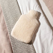 Load image into Gallery viewer, Hot water bottle cover made from sheepskin on a bed. 

