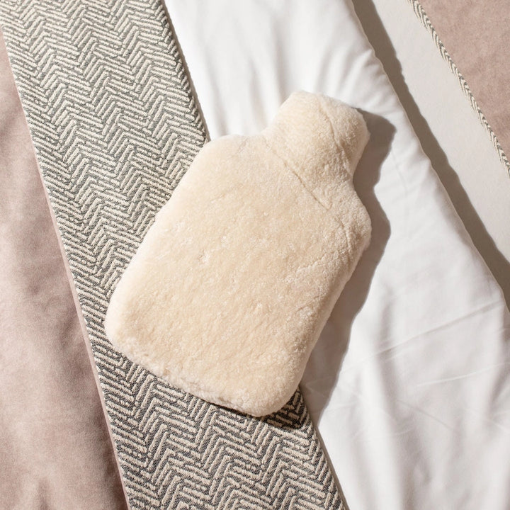 Hot water bottle cover made from sheepskin on a bed. 