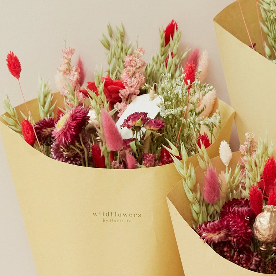 festive hand-tied field bouquet combines natural tones with striking reds, pinks, and copper hues for a passionate and lively touch. This bouquet contains: Natural oats, light pink phalaris, bordeaux lagurus, red phalaris, copper poppy, white limonium, dark pink helichrysum, lianne spray roses, bordeaux broom bloom, and red beetal.