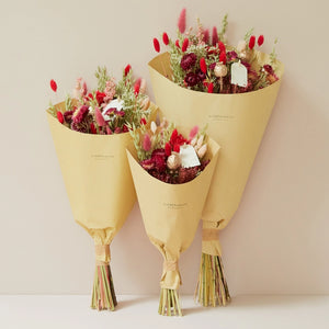 festive hand-tied field bouquet combines natural tones with striking reds, pinks, and copper hues for a passionate and lively touch. This bouquet contains: Natural oats, light pink phalaris, bordeaux lagurus, red phalaris, copper poppy, white limonium, dark pink helichrysum, lianne spray roses, bordeaux broom bloom, and red beetal.
